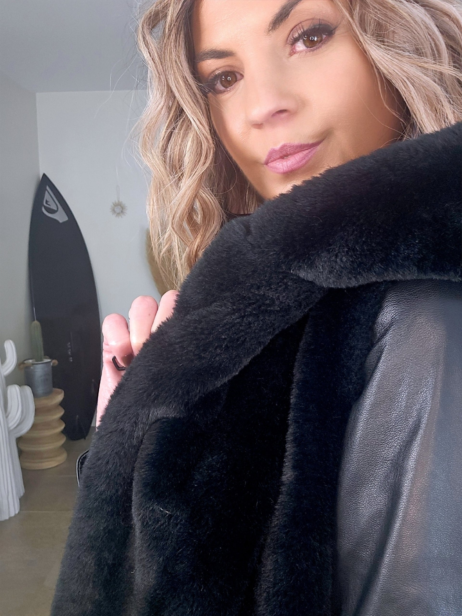 Manteau fausse fourrure noire à capuche sans manche.